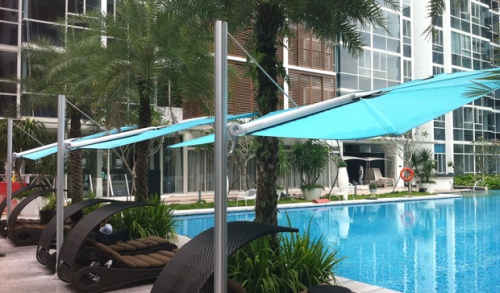 sp2590set spectra solo umbrella and paver base showing angled side view of three over lounge chairs on pool deck facing pool with landscaping trees and hotel in background