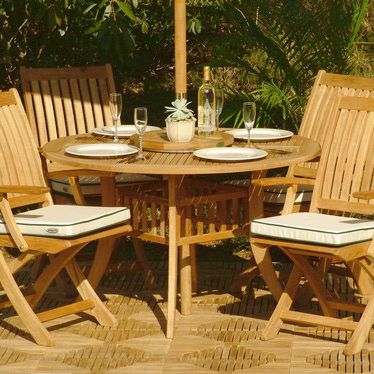 70043 Hyatt Barbuda 5 piece teak Patio Set with optional seat cushions and 4 place settings 4 wine glasses and bottle of wine on tabletop on Diamond Teak Tiles with trees in background