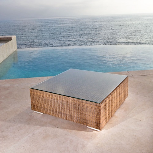 70242 malaga woven wicker coffee table with glass top top angle view on pool deck with infinity pool and ocean background