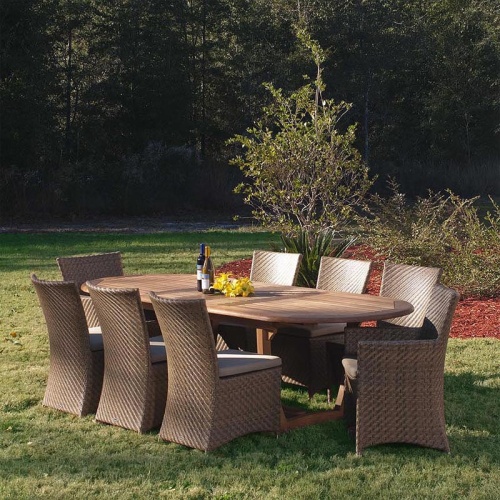 70244 Montserrat Valencia 9 Piece Dining Set on grass lawn showing 2 wine bottles and yellow flowers on top with landscape plants and trees in background