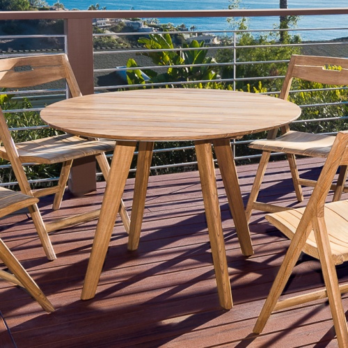 70519 Surf round teak 5 piece Dining Set closeup side view on wood deck with modern metal and wood balcony overlooking trees shrubs homes with ocean view