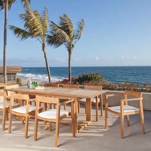 12901 Horizon 9 piece teak Dining Set of 8 teak armchairs with optional cushions and 60 inch rectangular dining table side view on concrete patio overlooking ocean with condo on left