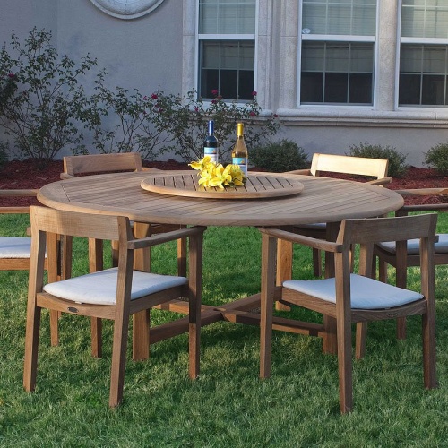 70238 Buckingham Horizon teak dining set with 2 wine bottles and yellow flowers on lazy susan in center of table and optional seat cushions on grass landscape plants and house in back 