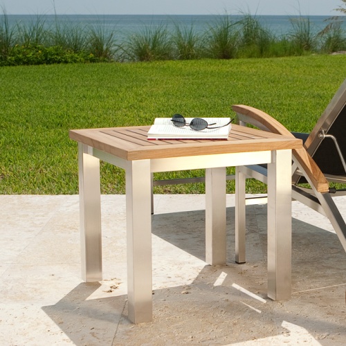 70779 Vogue teak and stainless steel side table with open book and sunglasses on table angled next to sling chair overlooking the ocean and blue sky