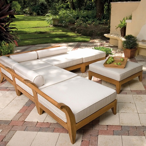 16766DP Aman Dais End Sectional set side view with bolsters and cushions a teak tray with green apples on an ottoman on an outside paver patio with potted plants and a lush background