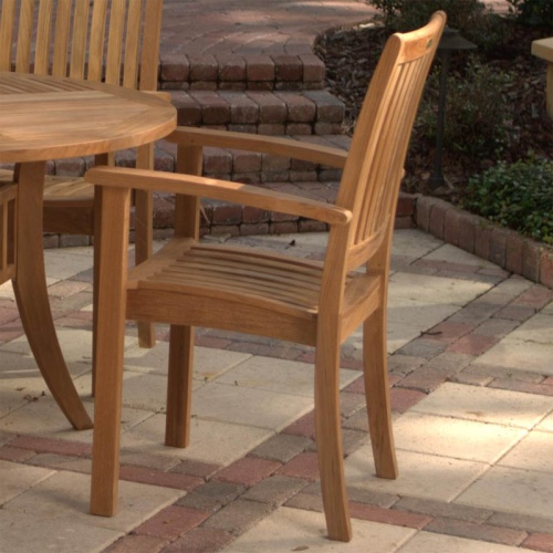 70027 Grand Hyatt teak Dining Set close view of armchair left side on brick patio with paver steps and shrubs in background
