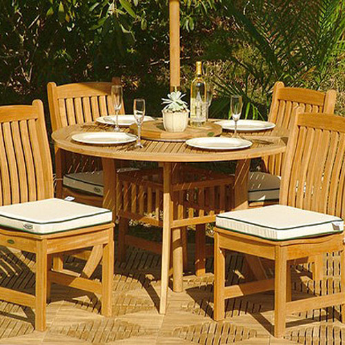 70040 Veranda Hyatt 5 piece teak Dining Set showing 4 place settings 4 wine glasses and wine bottle and plant in table center and optional cushions on teak tiles with shrubs in background
