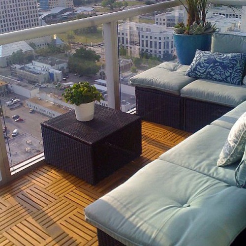 70409 parquet teak tiles one hundred cartons covering nine hundred ten square feet on condo balcony with glass railing potted palm and flowering plant a sofa set overlooking a city view 
