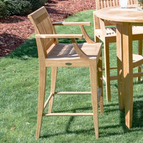 70632 Laguna teak Barstool with round teak table on grass lawn with mulch and shrubs in background