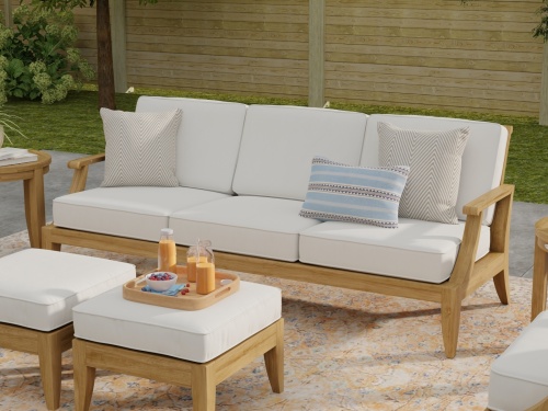 70871 Laguna 7 pc Conversation Set on patio showing closeup view of Laguna Sofa with throw pillows and 2 ottomans with tray of cereal and milk with fence and shrubs in background