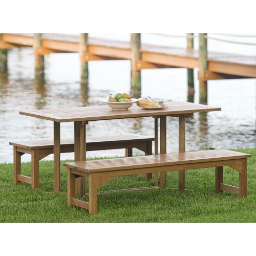 70061 Nevis Picnic Table Dining Set showing Nevis teak dining table and 2 teak Backless Picnic Benches with bowl of fruit bread on table in angled view on grass with water dock in back