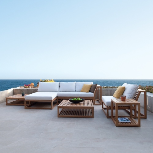 16800RFDP teak Maya Chaise Daybed shown with Maya left side sofa and Maya slipper chair on terrace with planters of landscape plants with ocean and blue sky background