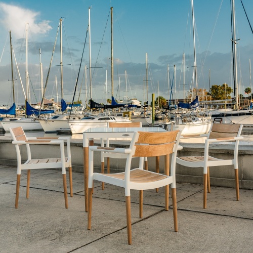  22916 Bloom Dining chair of 4 chairs around Bloom Square table on walkway with boats & yachts in marina and blue sky background