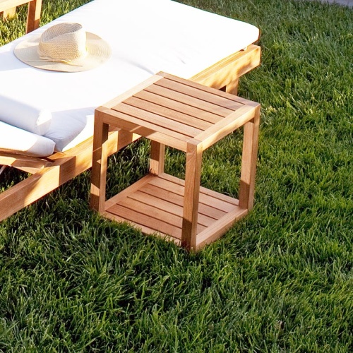 70309 Horizon teak chaise cushioned next to Horizon Teak Side Table showing close up view with hat on top of chaise on grass lawn