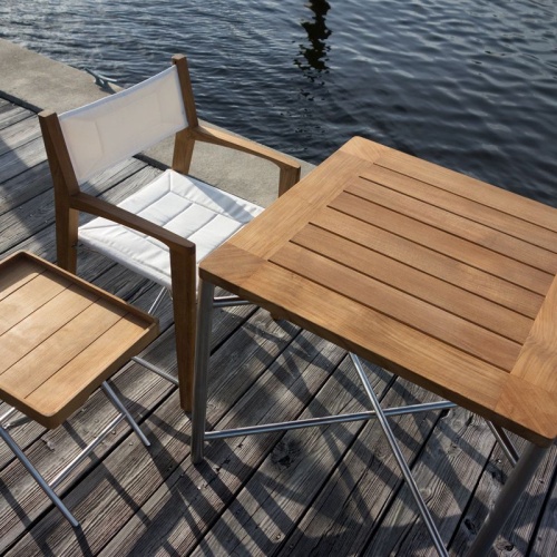 70460 Odyssey 3 piece Teak and Stainless Steel Set of Odyssey folding dining table and folding chair and folding ottoman with teak tray on wood deck and water in background