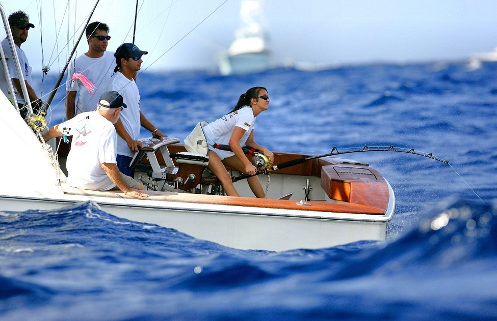 A side view image of people fishing at a Blue Marlin Tournament on a boat in the ocean.