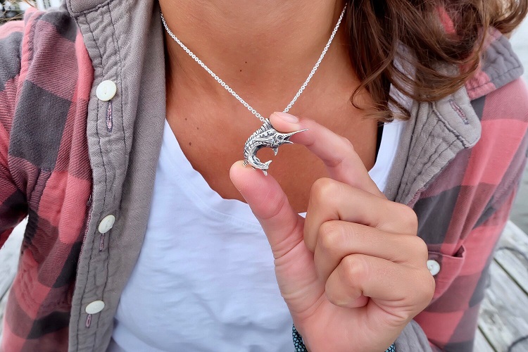 Closeup view of The Billfish Foundation necklace on a woman wearing a white t-shirt and red and black plaid shirt.