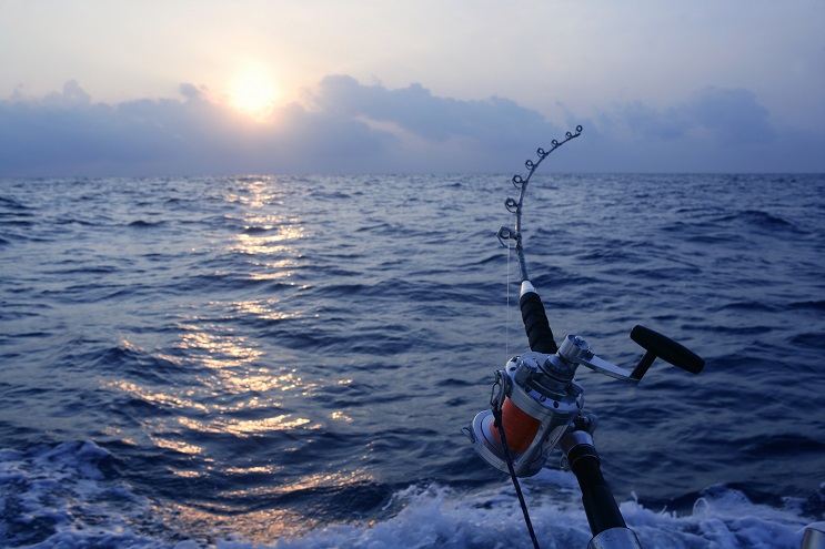 An image of a fishing pole on an Angler big game fishing  boat in the ocean with the sun low on the horizon.