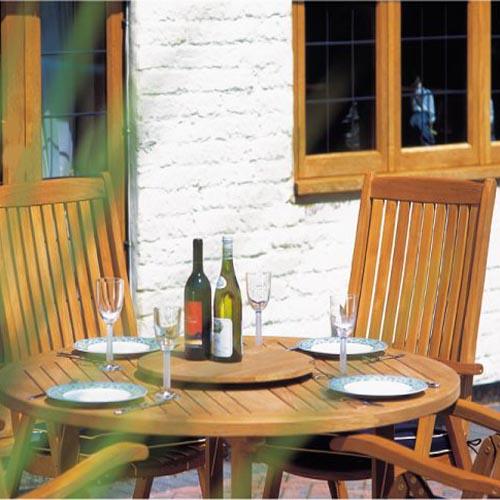 alt="70028 Barbuda Reclining 5 pc Teak Set showing closeup side view with 4 place settings 4 wine glasses and wine bottle on lazy susan with  house windows and glass door in background"