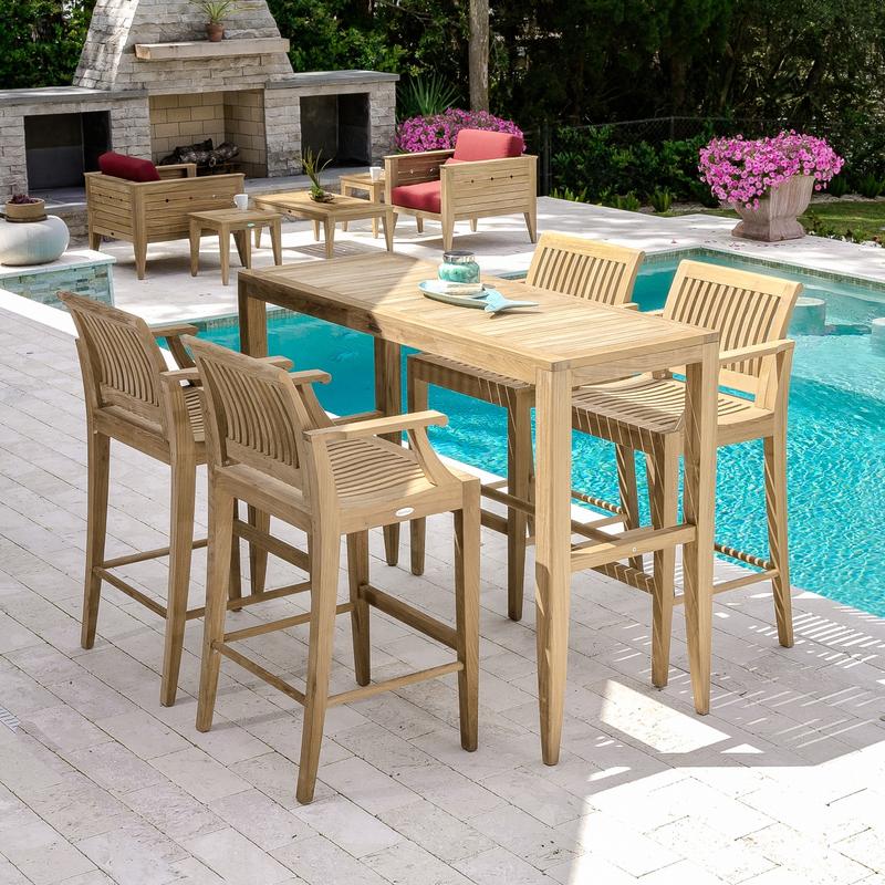 alt="15821 Laguna 5 foot Teak Bar Table and 4 barstools on patio stones by pool with fireplace two potted flowering plants two teak Craftsman Chairs and shrubs in background"