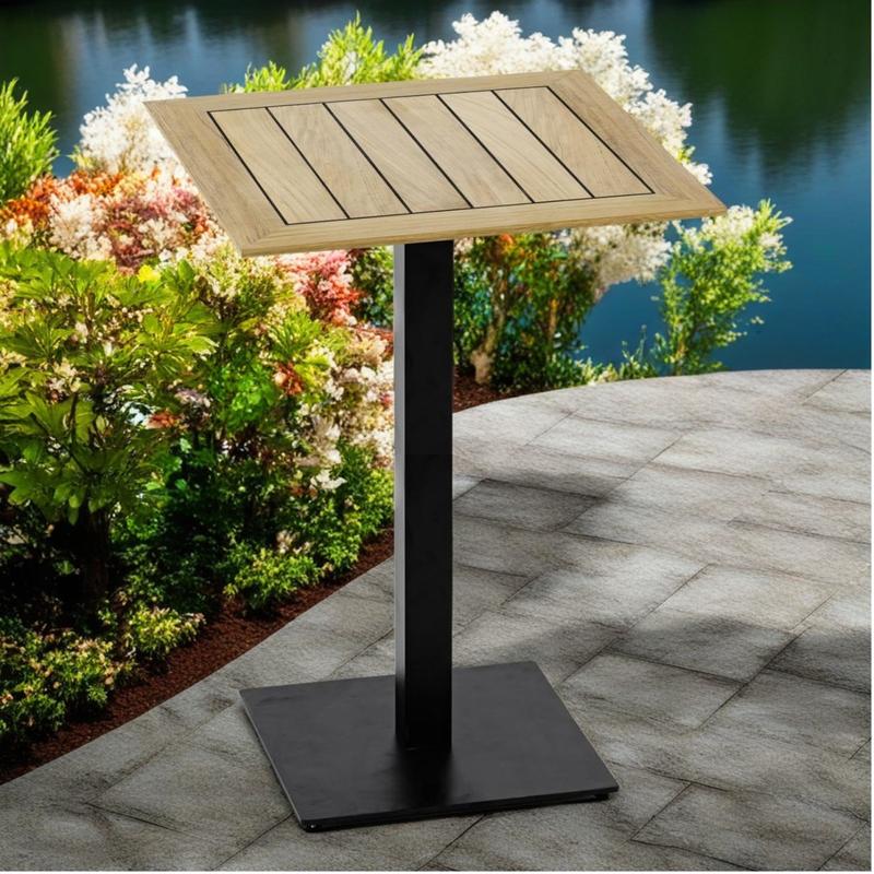 alt="70835 Vogue 42 x 42 inch Bar Table top with sikaflex marine sealant between teak slats on paver patio surrounded by flowering shrubs and lake in background"