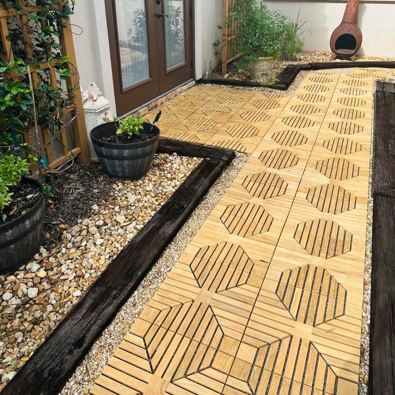 alt="18408P diamond teak tiles assembled on a walkway leading to a door with landscaping rocks and plants on each side and chimenea against a wall in background "