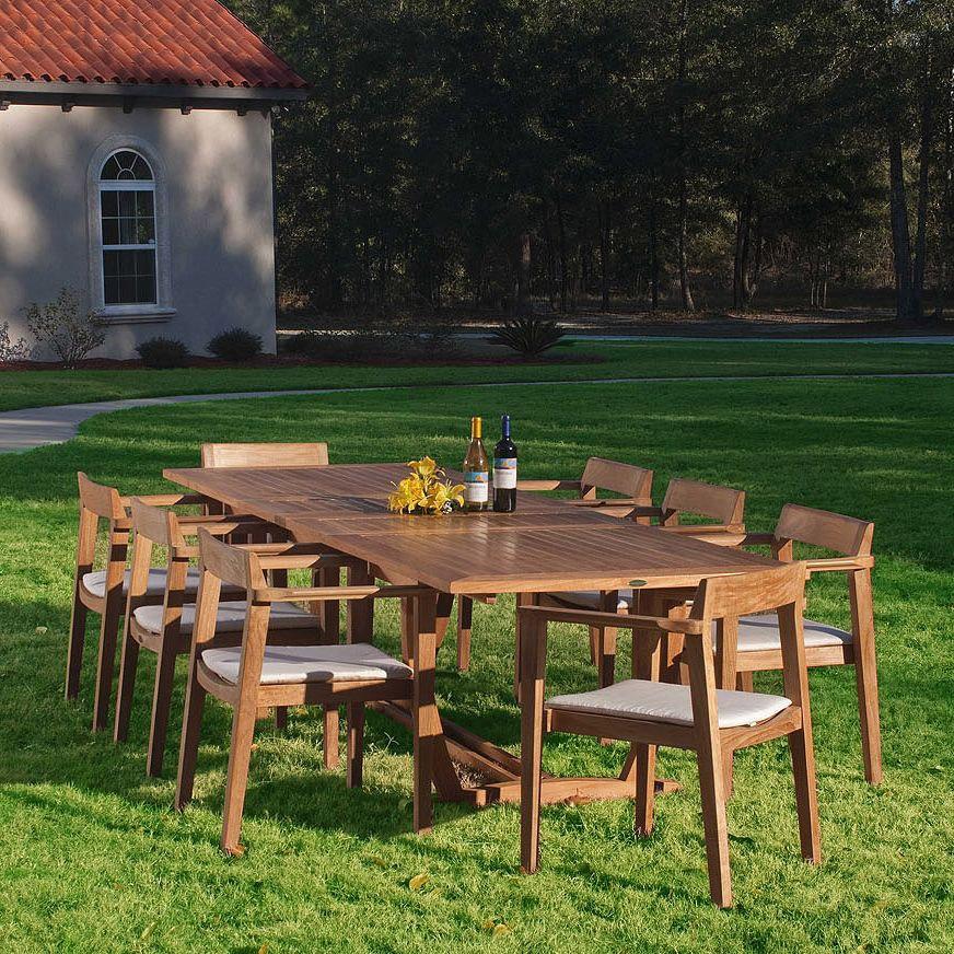 70237 Grand Horizon teak 9 piece Dining Set with optional canvas colored cushions yellow flowers two wine bottles on grass lawn house and landscaped background