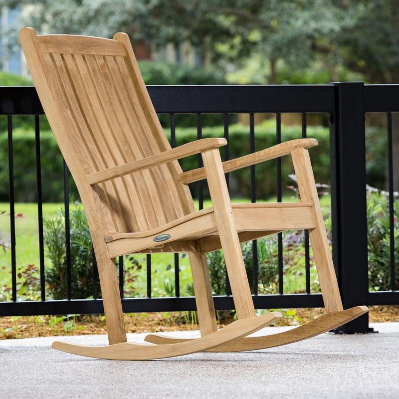 alt="12223 Veranda Teak Rocking Chair on porch in side view with railing and landscaped lawn in background"