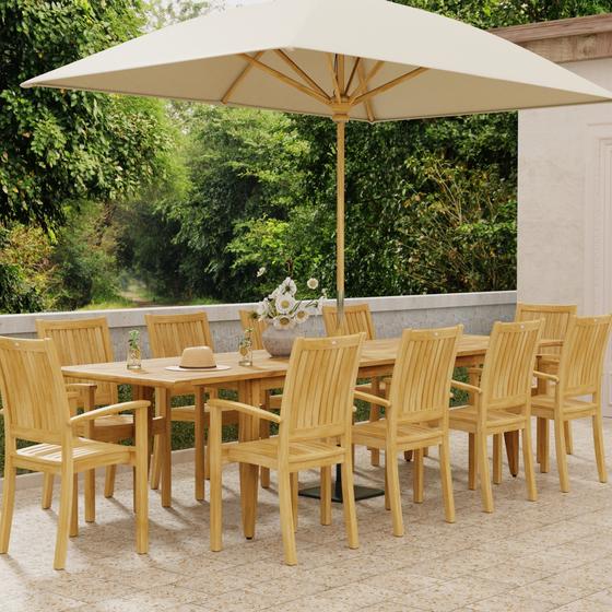 70812 Laguna Sussex teak 11 piece Dining Set with 2 water glasses a vase of flowers with open rectangular umbrella on outdoor terrace with trees and house in background
