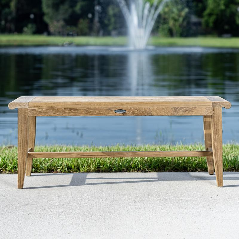 alt="13915 Laguna 4 foot long teak Backless Bench on concrete walkway with grass and lake with fountain in background"