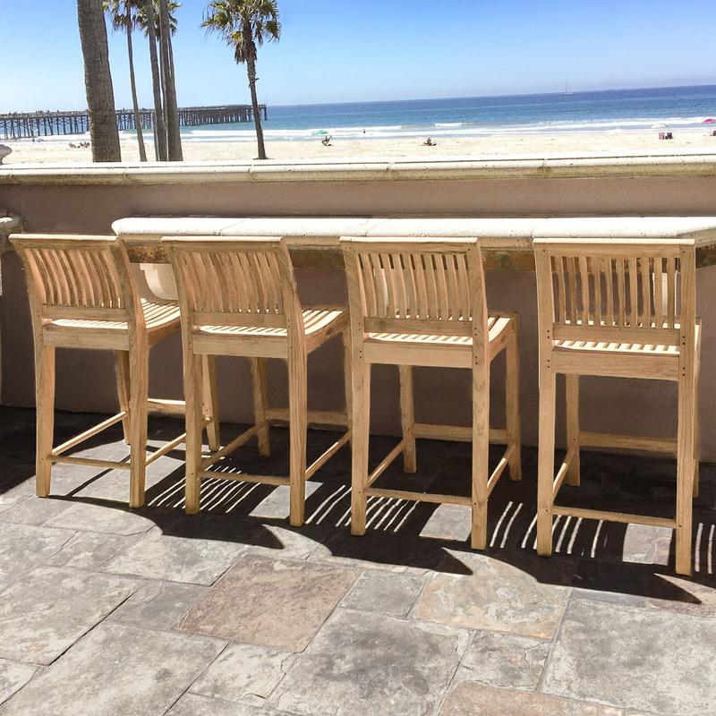 alt="70760 Laguna Teak Counter Stools Set of 4 on tiled stone patio against a counter overlooking the ocean with palm trees sandy beach ocean pier blue sky background"