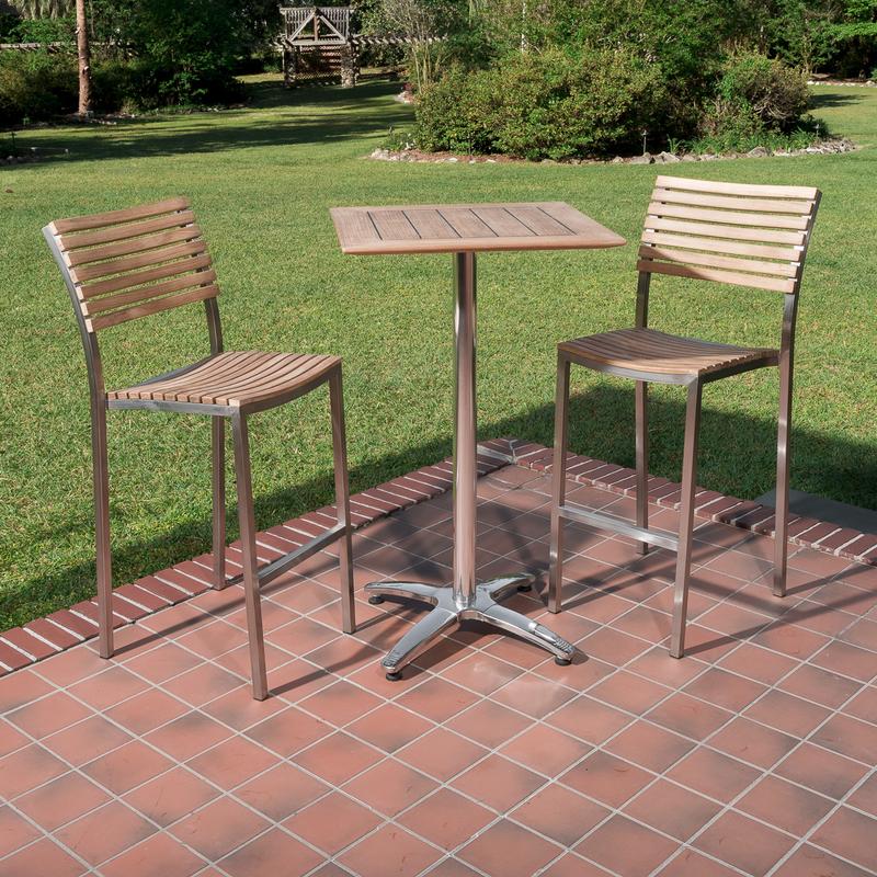 alt="70673 Vogue teak and stainless steel High Bar Set of 2 barstools and 24 inch square teak table on brick paver and tiled outdoor patio with grass and landscape plants in background"