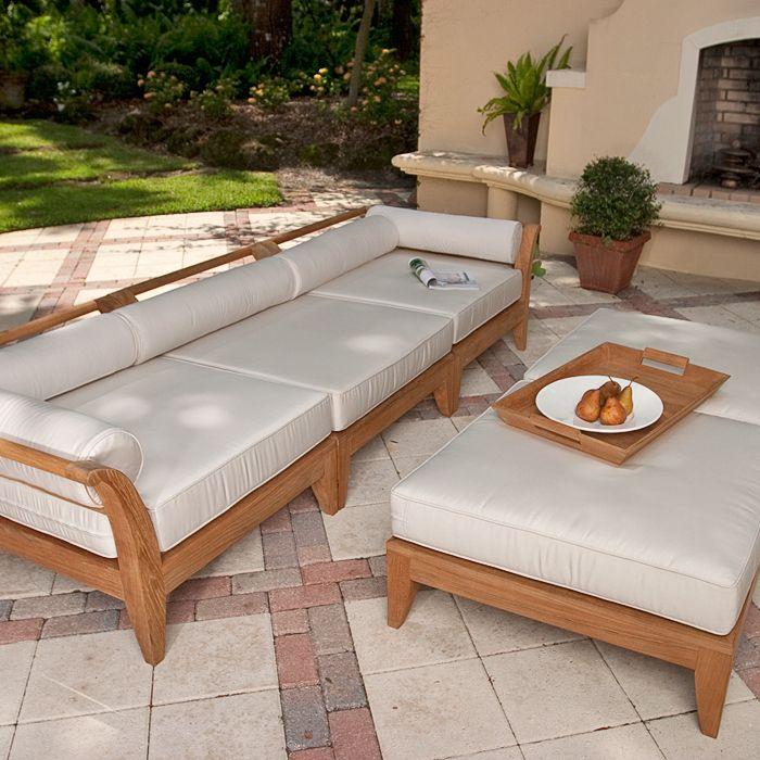 alt="thumbnail image of 70102 Aman Dais 3 pc Sofa Set cushioned with magazine and two optional ottomans with plate of pears on teak tray set on patio with fireplace two plants grass and treed background "