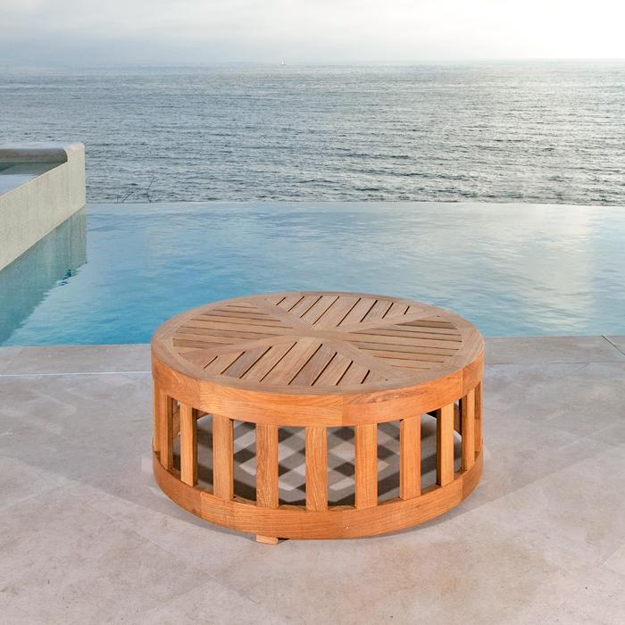 alt="14171 Kafelonia 36 inch Teak Coffee Table Ottoman Frame side angled view on stone patio with an infinity pool ocean and blue sky in background"