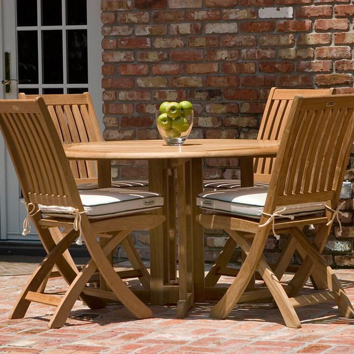 alt="70036 Barbuda teak 5 piece round Dining Set on brick patio showing glass bowl of green apples on table and optional seat cushions with windows and brick house in background"