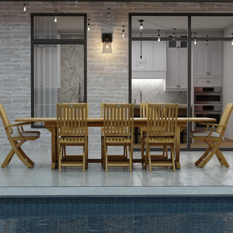 alt="70794 Veranda Barbuda Teak 9 pc Dining Set of Grand Veranda Dining Table and 2 Barbuda Armchairs and 6 Side Chairs side view on a patio with patio lights and glass doors in background"