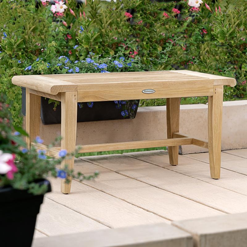 alt="13068 Laguna teak 3 foot long Backless Bench on a stone walkway a potted blooming plant in front with shrubs and  flowering plants in background"