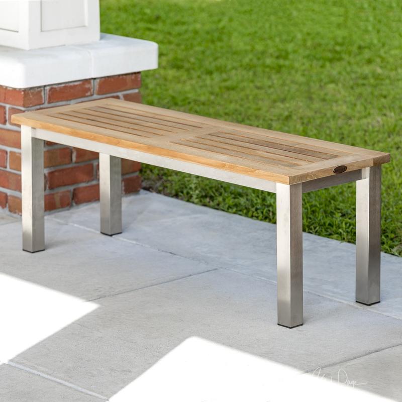 alt=" 23940 Vogue teak and stainless steel 4 foot backless bench on concrete walkway with grass in background"