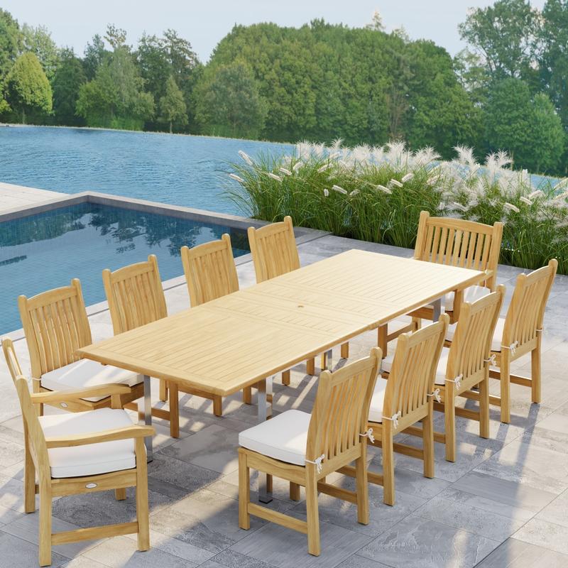 alt="70826  Vogue Veranda 13 pc Teak Dining Set with optional seat cushions showing angled end view on patio next to a pool with plants and a lake with trees in background"