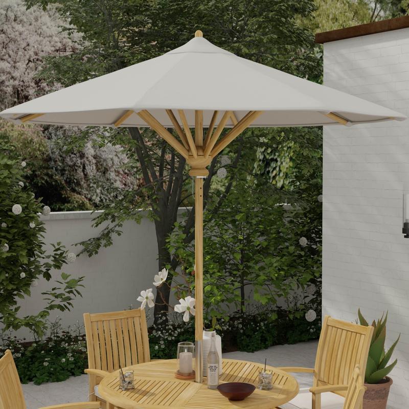 alt="17540F Somerset 8 foot Round teak Umbrella extended on round teak dining set with 2 glasses and white flowers in vase a candle and bowl on tabletop with landscape plants and house in background"