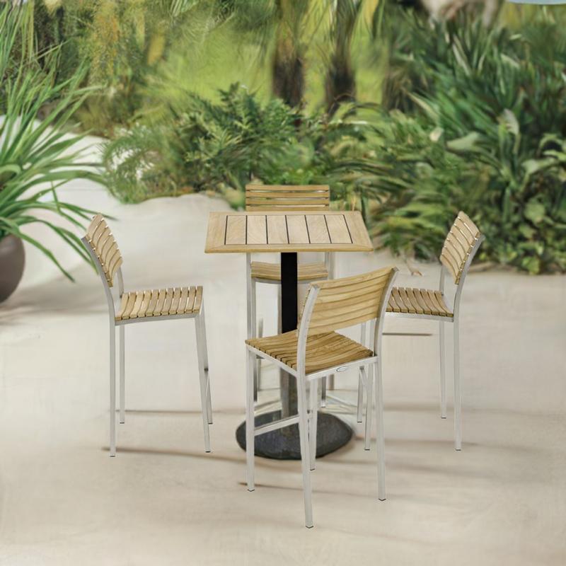 alt="70687 Vogue 5 pc Bar Furniture Set of a Teak 30 inch Square Table Top on black base and 4 Vogue Teak and Stainless Steel Barstools aerial side view on patio with plants in background"
