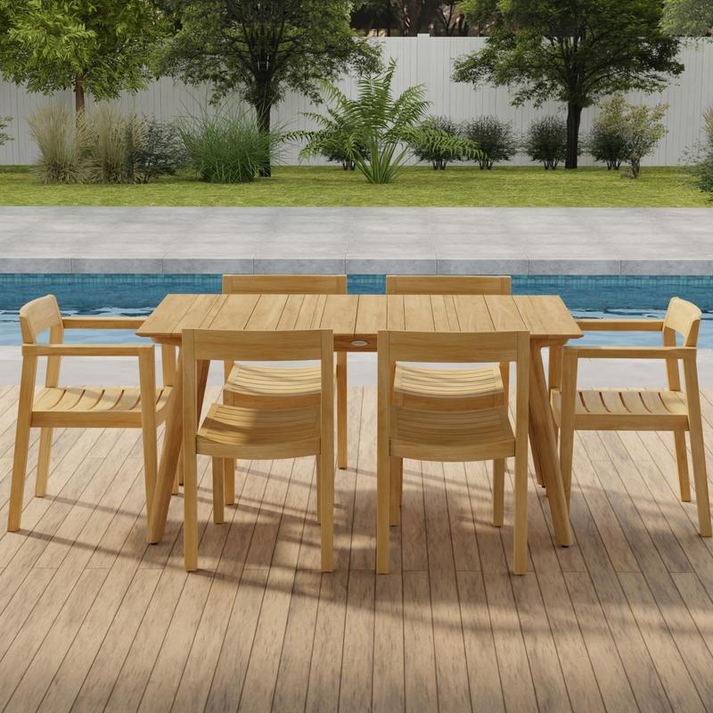 alt="70525 Surf Horizon 7 pc Dining Set of a Surf Teak 60 inch Rectangular Table angled side view on patio in front of a pool with grass and landscaping plants and trees and white fence in the background"