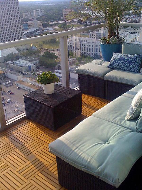 alt="70406 Parquet 10 pack Teak 18 inch Deck Tiles on outdoor balcony with sectional sofa and side table with plants overlooking a city "