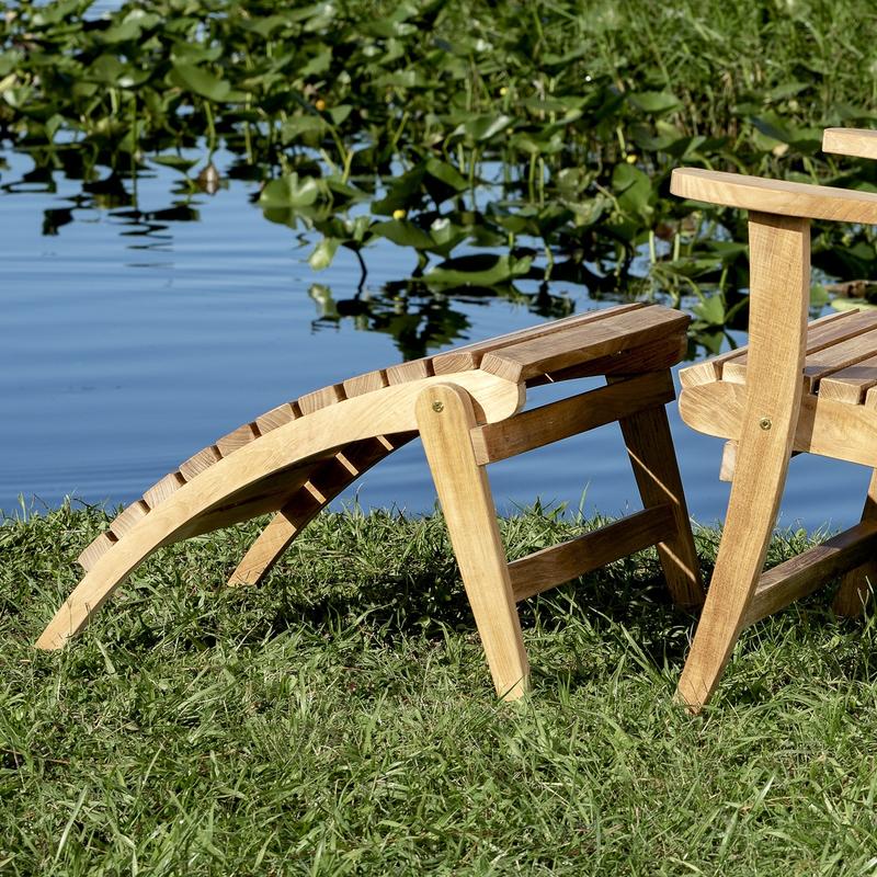 alt="18607 adirondack teak footrest ottoman back angled view on grassy bank with water plants and water view"
