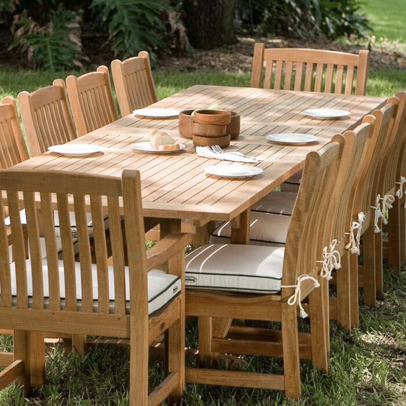 alt="70017 Grand Veranda 13 piece dining set with optional seat cushions a plate of bread serving plates and wooden bowls on a green lawn and lush landscape background"