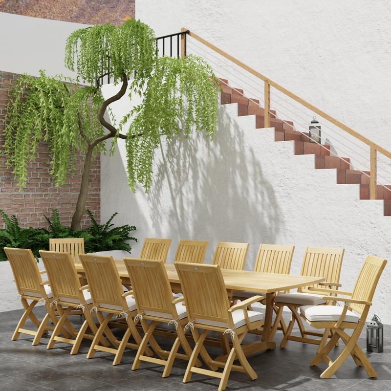 alt="70095 Barbuda Teak 13 pc Patio Set of a Barbuda 10 foot rectangular extension table and 12 folding reclining armchairs in angled with plants next to a staircase in background"