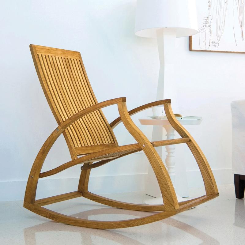 alt="16419 Aria Teak Rocker against white wall with artwork sitting on marble floor next to white side table and lamp in an inside room"