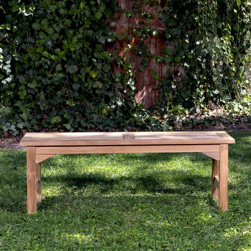 alt="13940 Veranda 4 foot Teak Backless Bench side view on grass area with trees & shrubs in background"