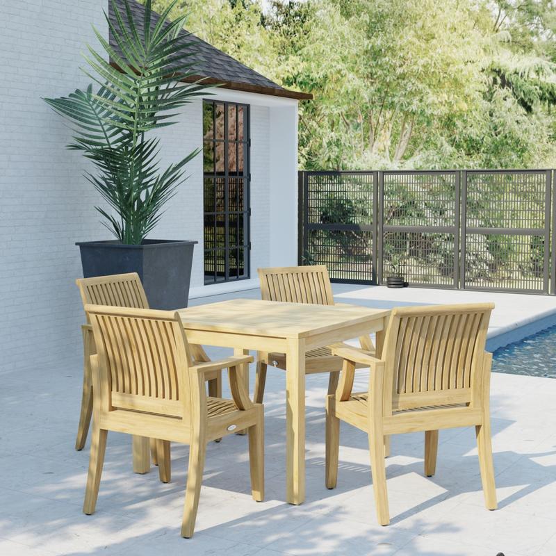 alt="70555 Laguna 5 pc Square Dining Set of Bistro 36 inch Square Teak Dining Table and 4 Laguna Dining Armchairs in corner view on patio next to a house and fence in the background "