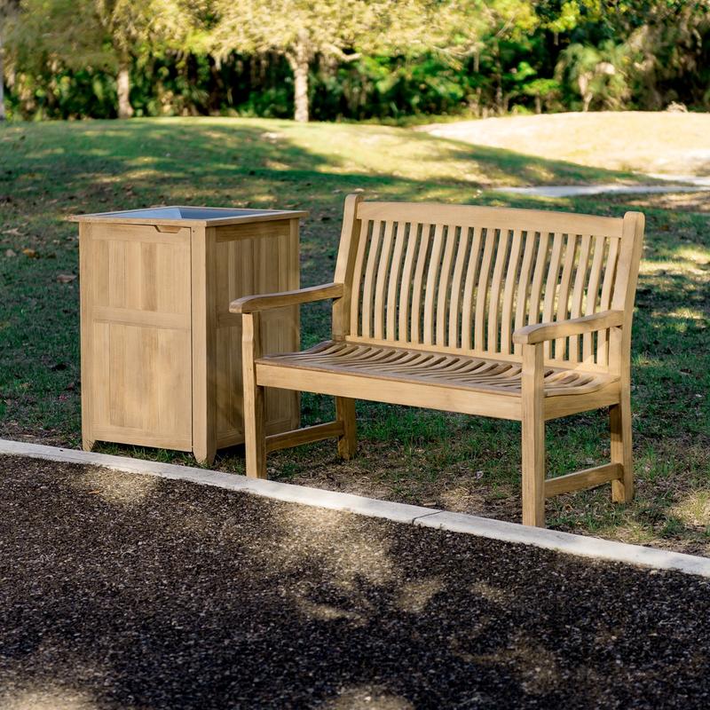 alt="13218 Veranda Teak 4 foot Bench beside trash receptacle on grass field with garden in front and trees in background"